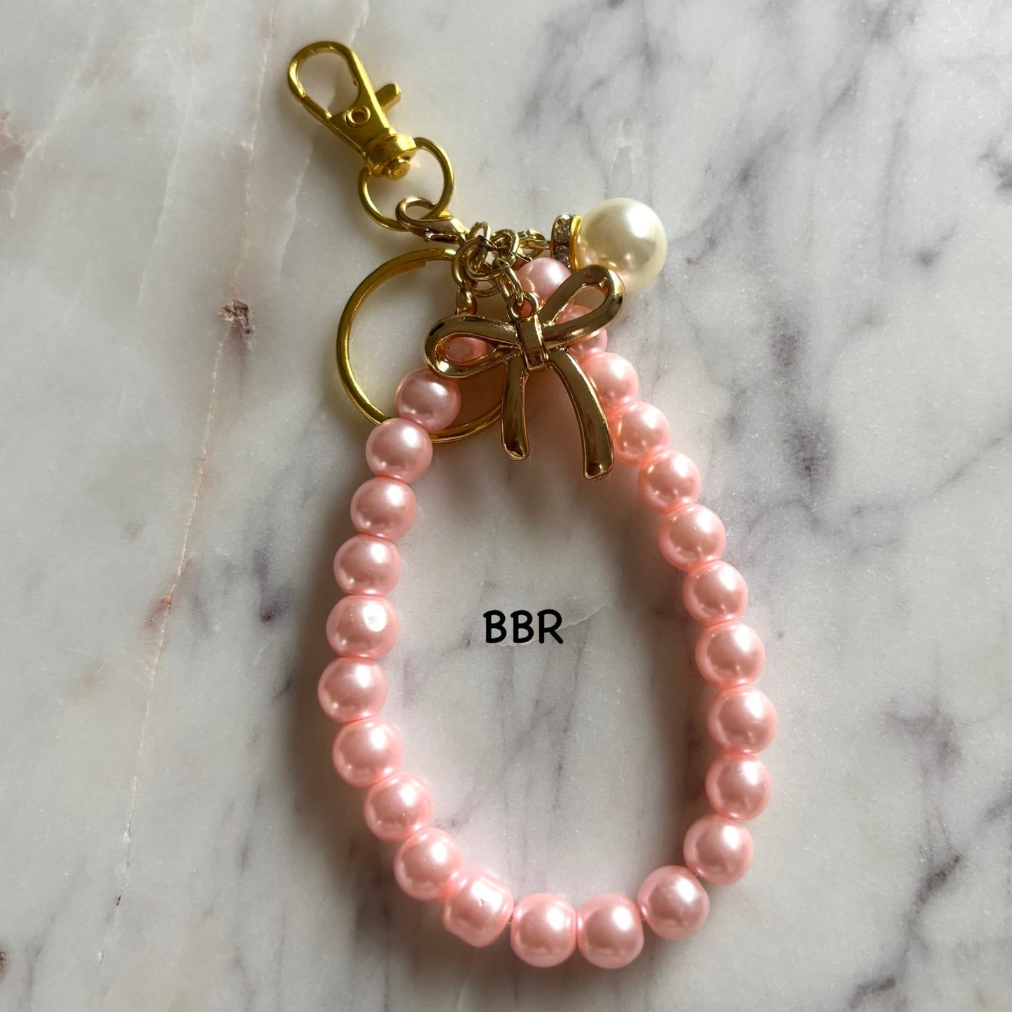 Pink pearl keychain with a gold bow charm.
