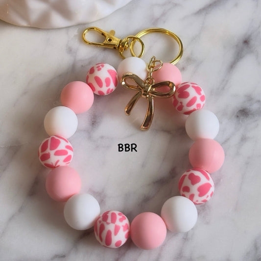 Handmade wristlet beaded keychain with pink and white silicone beads and a gold bow charm.