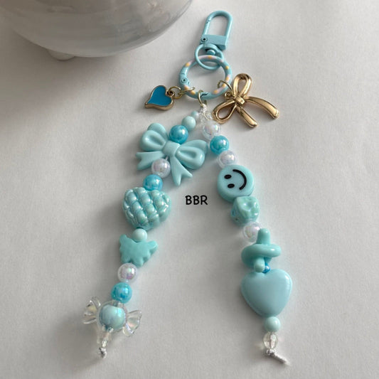 Handmade baby blue beaded bag charm with a beautiful baby blue bow bead, a gold bow and blue heart charm on a baby blue swivel snap hook for easy attachment.