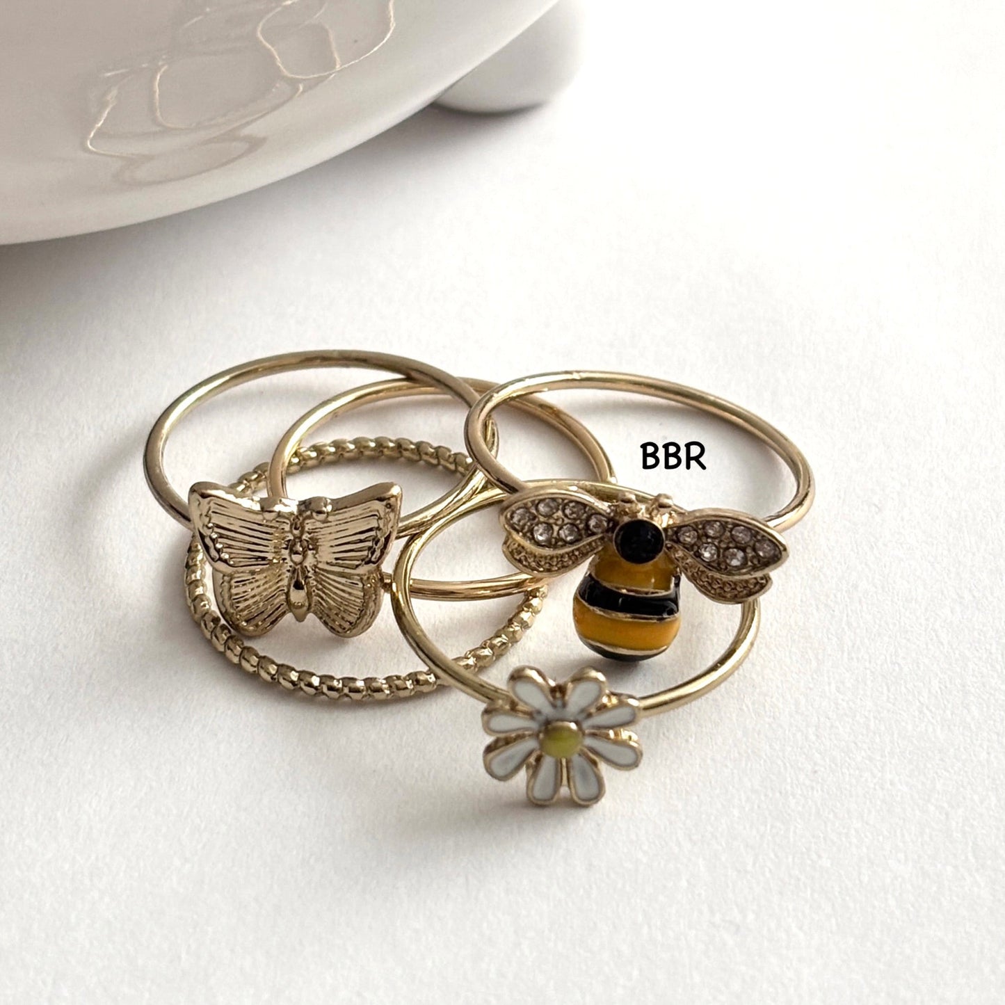 A 5-piece gold tone stacking ring set featuring a butterfly, bumble bee, daisy, twisted band, and slim band.