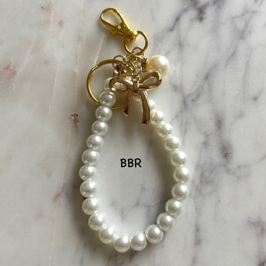 Pearl keychain with a gold bow charm.